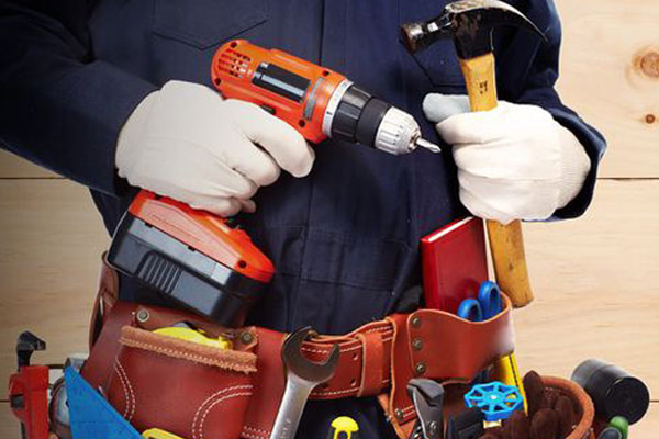 handyman wearing a tool belt and holding a drill and hammer